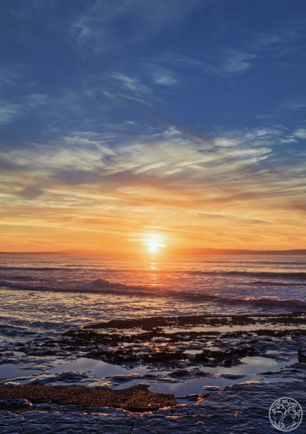 A golden sunset over the Atlantic Ocean at Enniscrone Beach, County Sligo, featuring rock pools and gentle waves.